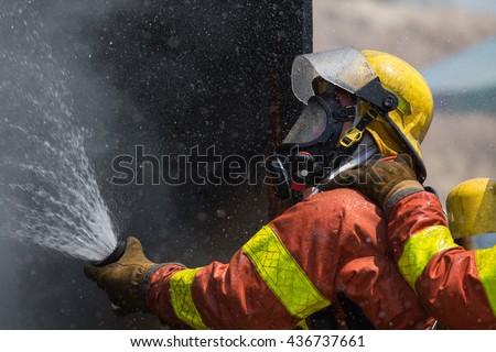 fireman in helmet and oxygen mask  spraying water to fire surround with smoke and drizzle