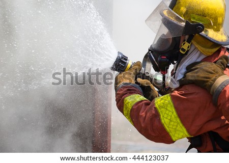 fireman in fire fighting suit spraying water to fire surround with smoke and drizzle