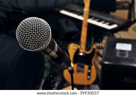 in a rehearsal room from a pop band. a microphone in the front. in the background a guitar and a keyboard are visible
