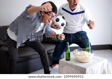Young Happy Asian Men family or football fans watching soccer match on tv and cheering football team, celebrating with drink beer and eat popcorn at home, sports and entertainment concept.