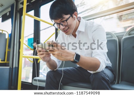 Young Asian man traveler sitting on a bus using smartphone watch video or playing game while smile of happy, transport, tourism and road trip concept.