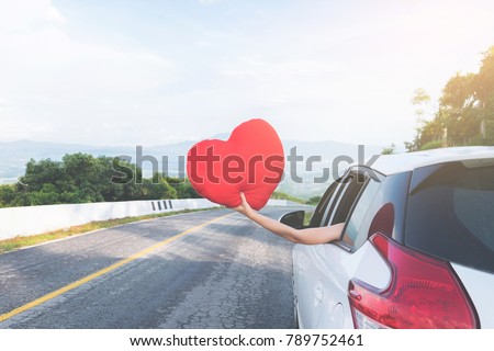 Relaxed happy traveler, Young beatiful asian gilr holding red heart and Reach out of the car at sunset and beautiful view with mountain road background.