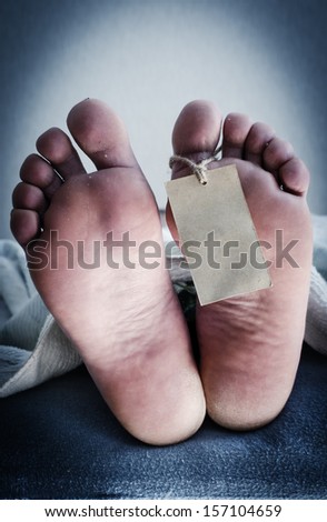 Two feet of a dead body, with an identification tag. Blue toned.