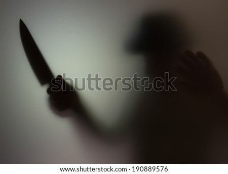 Shadowy figure with a knife behind glass