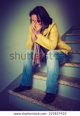 Sad woman sitting on the stairs in the entrance of a house. LOMO style