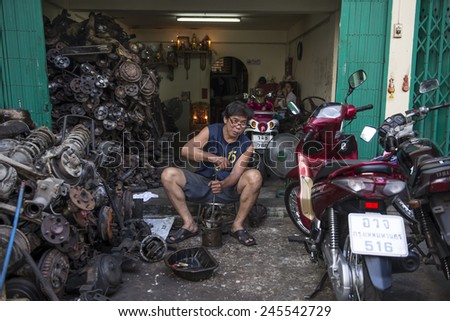 BANGKOK, THAILAND - DECEMBER 25, 2014: Street Photography of owner of a small body shop repairs scooter.