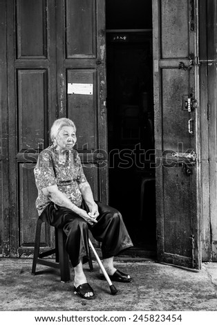 BANGKOK, THAILAND - DECEMBER 25, 2014: Street Photography of old woman with a cane in her hands sitting on a chair near the door of her house