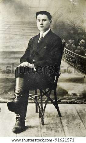 RUSSIA - CIRCA 1912: Old photo printed in Russia shows young man sitting on a chair, circa 1912