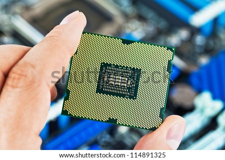 Macro view of modern multicore CPU processor in human hand with PC computer motherboard in background. Selective focus DOF effect