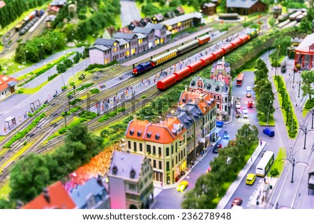 Macro view of toy hobby railroad layout with railway station building, passenger and freight cargo trains on rail tracks