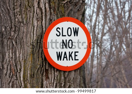 Slow no wake sign nailed to a tree