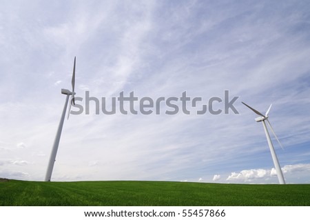 two windmills in a green meadow cloudy sky