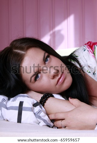 Beautiful young woman lying in bed with her arm under her head in a pink bedroom