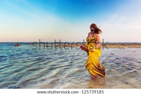 Beautiful woman walking in water wearing a yellow colorful dress