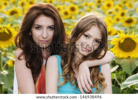 Portrait of a beautiful two happy young women with long hair in sunflowers field