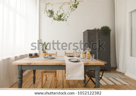 Cozy interior of kitchen with wooden table and cupboard and green plants in decor.