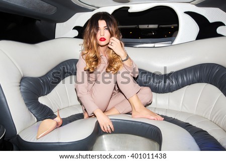 Woman in a pink business suit with bright makeup and shoes with heels sitting on car limousine interior