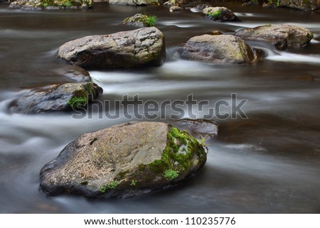 streaming water between big rocks river flow with long exposure giving smooth water surface, strong current