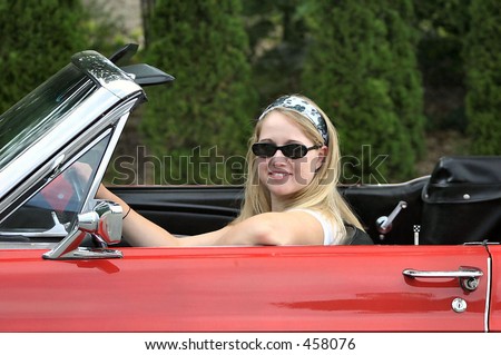 young blonde lady behind the steering wheel of a red antique convertible sports car