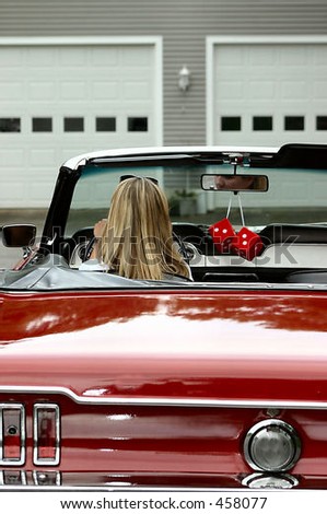 young blonde lady sitting behind steering wheel of red antique convertible sports car