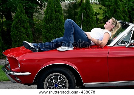 young blonde lady relaxing on hood of red antique convertible sports car