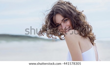 Happy woman on the beach. Portrait of the beautiful girl close-up, the wind fluttering hair. Autumn portrait on the beach.