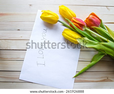 Yellow and orange tulips on a wooden table and a piece of paper with the words I love you