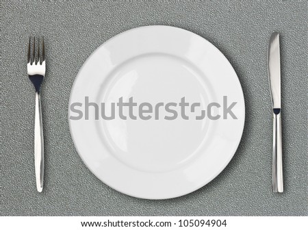 White plate, fork and knife top view on gray plastic textured table surface