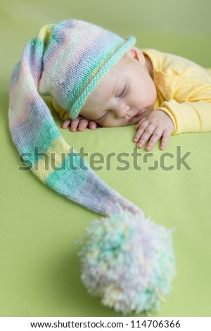 sleeping baby in funny hat on green background