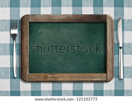 Menu blackboard lying on tablecloth with knife and fork