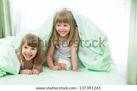 Two little girls lying under blanket on bed