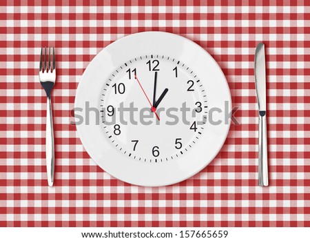 Knife, white plate with clock face and fork on red picnic table cloth