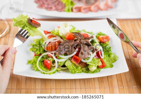 Vegetable salad with beef meat and persons hands with fork and tableknife