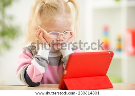 happy child in glasses looking at mini tablet pc screen sitting at table