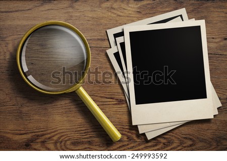 magnifying glass or loupe with old polaroid photo frames stack on wood table