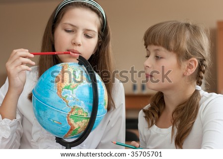 Two schoolgirls search geographical location using globe