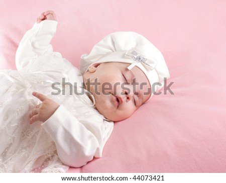 Little 3 months baby-girl sleeping on pink sheet dressed in white suit