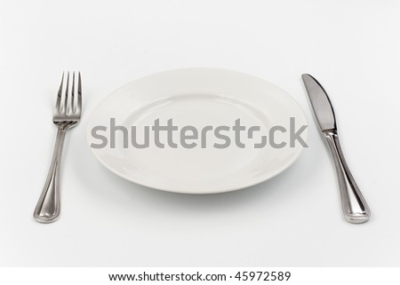 Place setting for one person. Knife, white plate and fork.