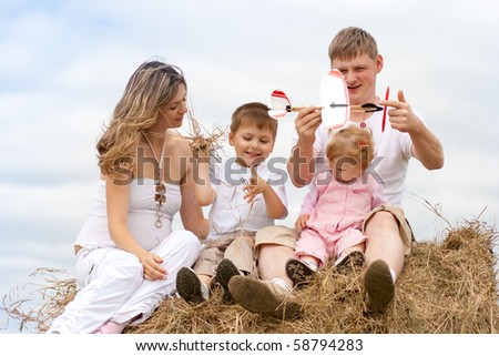 Happy family launching toy aircraft model sitting on haystack together