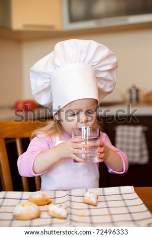 Little baker or cook girl drinks water on kitchen
