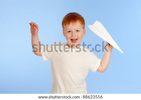 Adorable red-haired boy with paper plane model on blue background in studio