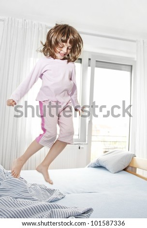 happy little girl jumping on a bed after waking