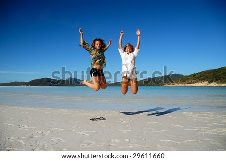 Two beautiful young women jumping on beach with clear sky and ocean in background