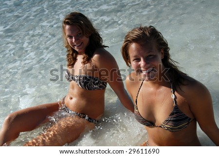 stock photo Two sexy young girls in bikini sitting in the water at beach 