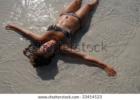 Cute teenage girl lying in water on a beach doing snow angel