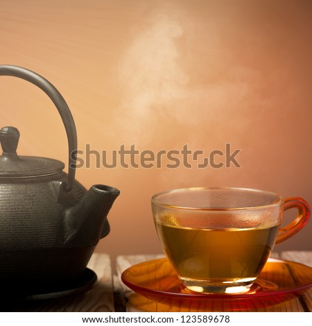 Teapot and a cup of tea on an old wooden table - hot steam smoking from cup of tea