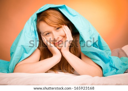 Woman lying on pillow in bed, covered with blue blanket