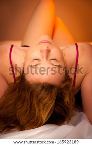 woman in lingerie lying on satin sheets bed in bedroom
