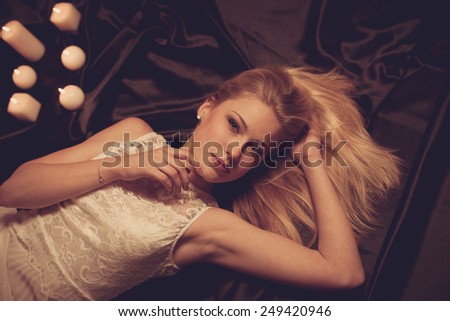Young blonde woman on black sheets with candels in background