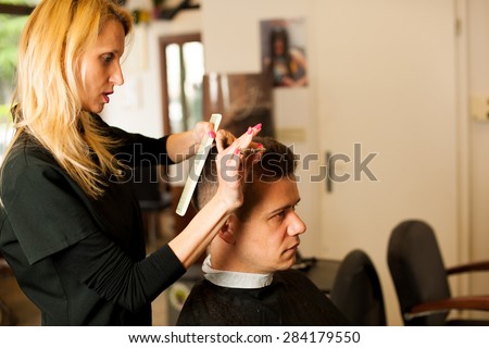 Female hairdresser cutting hair of smiling man client at beauty salon